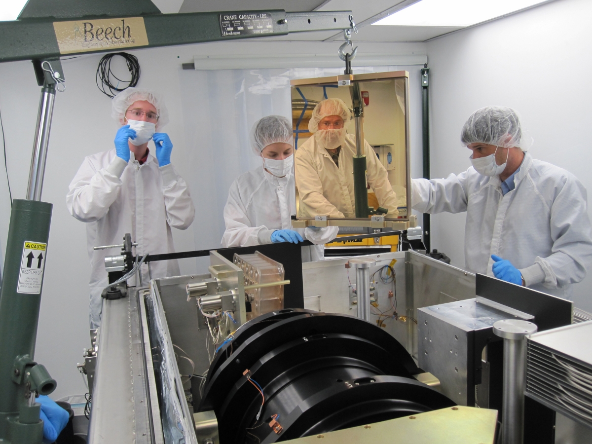 A photo of four SDSS-III scientists working on the APOGEE spectrograph.  Left to right: Garrett Ebelke (Apache Point Observatory), Gail Zasowski (The Ohio State University), Steven Majewski (University of Virginia) and John Wilson (University of Virginia). Majewski is actually standing across the room; he appears here as a reflection in a mirror that was being installed in the spectrograph.  Image credit: Dan Long (Apache Point Observatory)